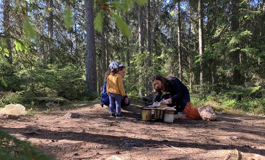 Två kvinnor och ett barn vid en eldstad i skogen