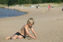 Pojke sitter på sandstrand.