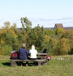 Två personer sitter vid rastbänk med utsikt mot Gamla Uppsala kyrka.