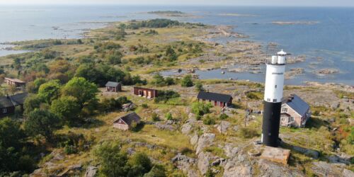 Flygbild över en ö i havet. På ön syns klippor, träd, en fyr och några hus.
