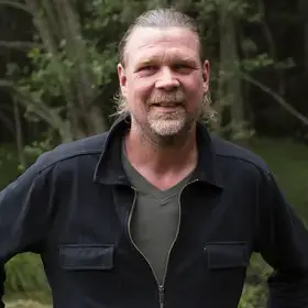 En man som heter Henke Jonsson och är tillsynsperson står framför en träddunge.