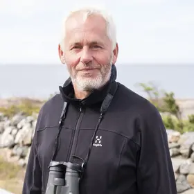 En man som heter Lennart Söderlund står med havet och en stenmur bakom sig.