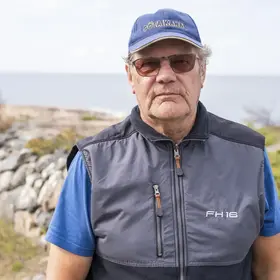 En man som heter Bengt-Olov Jansson och är tillsynsperson står framför en stenmur och med havet bakom sig.