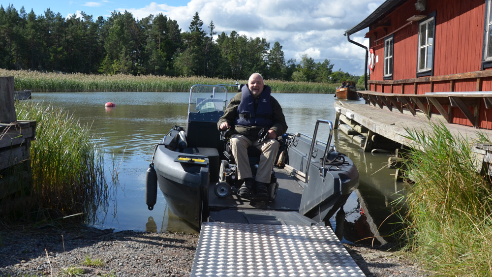 En person i rullstol är på väg att åka från en båt över till en ramp på stranden.