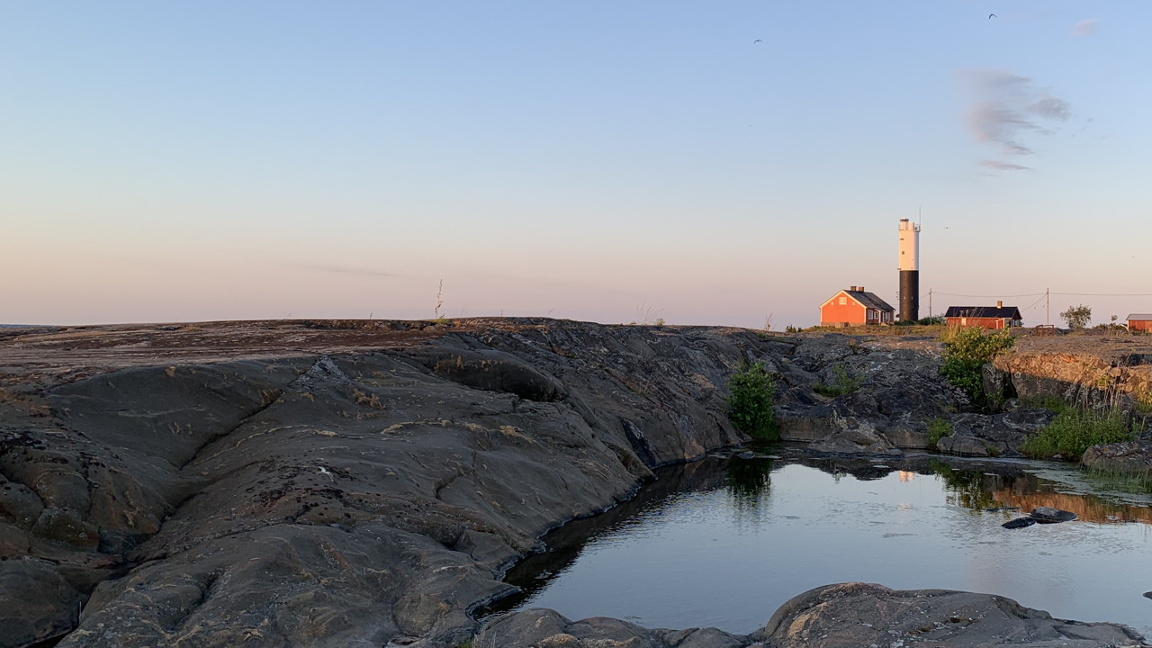 Hus med fyr på klippor i solnedgång..>