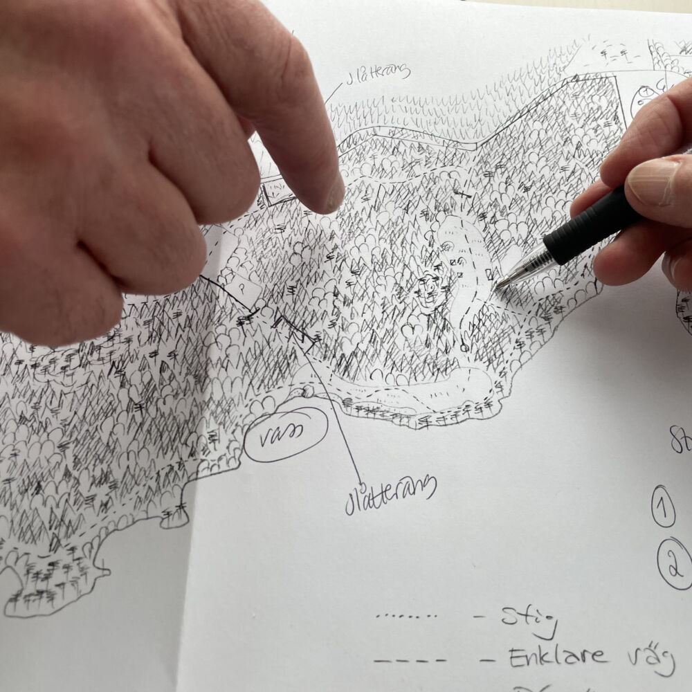 Närbild på två händer, den ena håller i en penna och ritar på en kartskiss, den andra pekar på skissen.