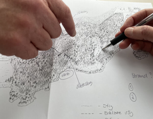 Närbild på två händer, den ena håller i en penna och ritar på en kartskiss, den andra pekar på skissen.