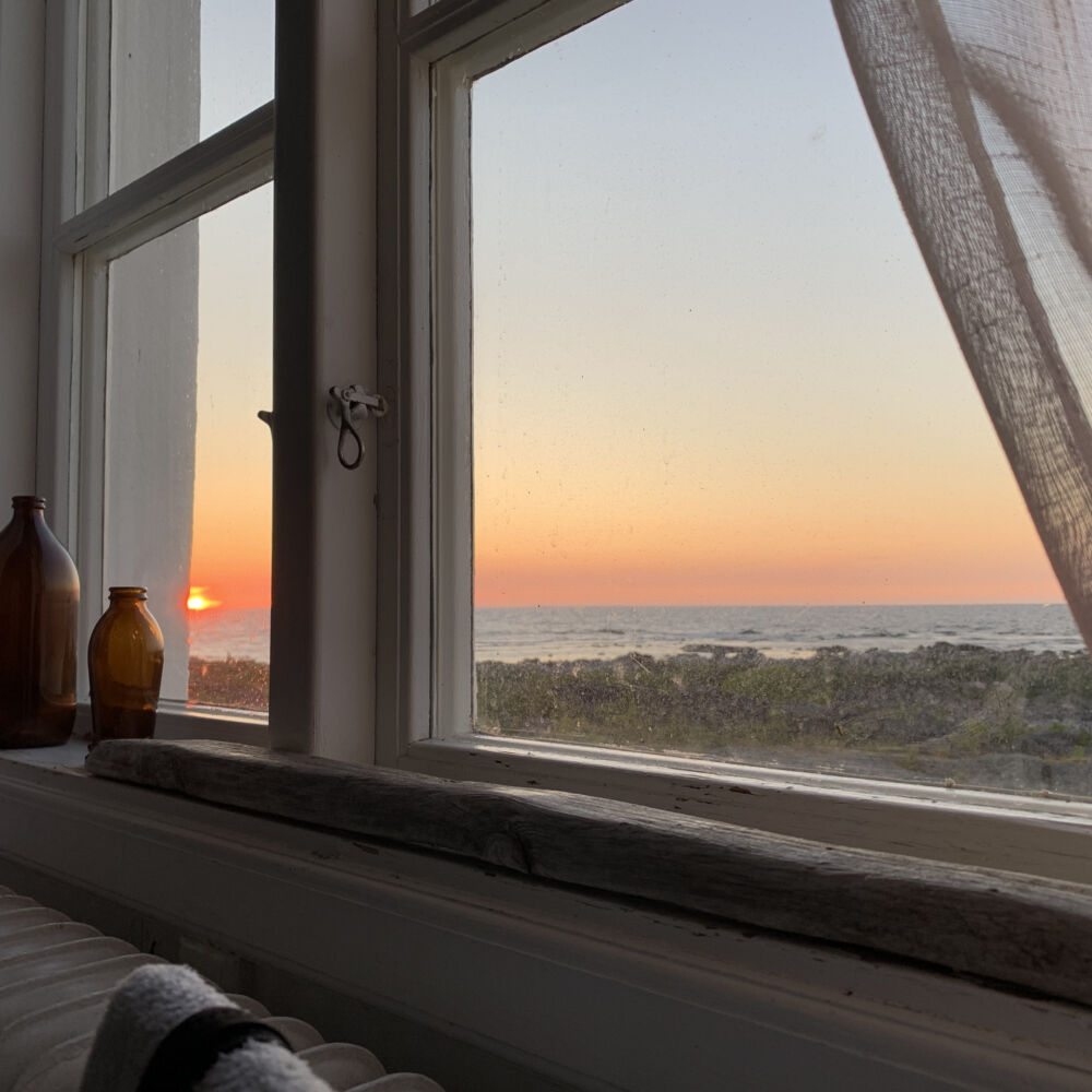 Utsikt över en solnedgång över havet, genom ett fönster.