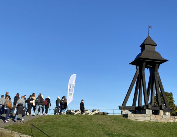 Klockstapel i mitten, trappor, en skolklass och en flagga.