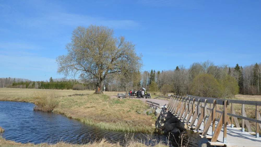 En å rinner genom ett öppet landskap och en gångväg passerar över ån på en gångbro.