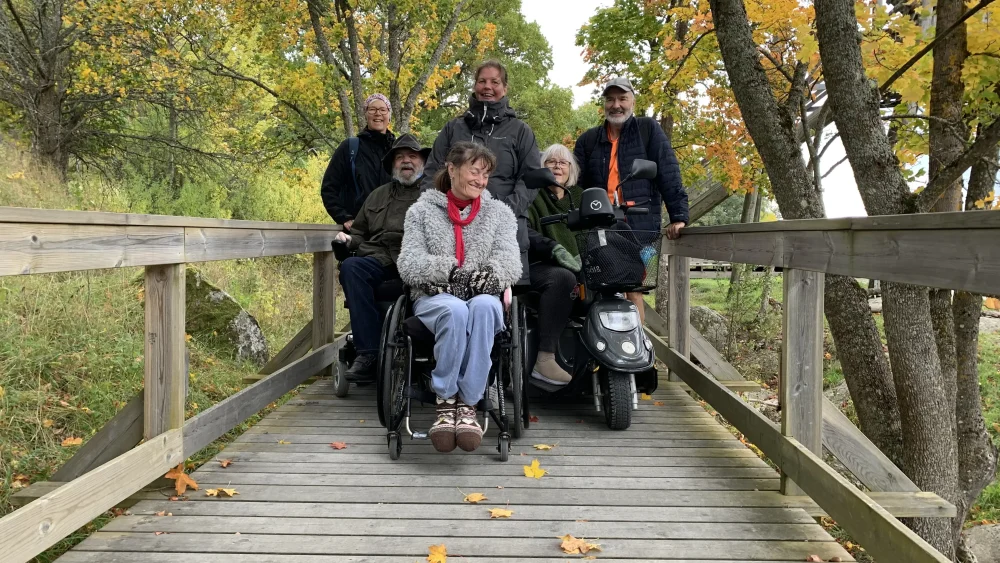 En grupp människor på en bro i en park, flera av dem sitter i rullstol.