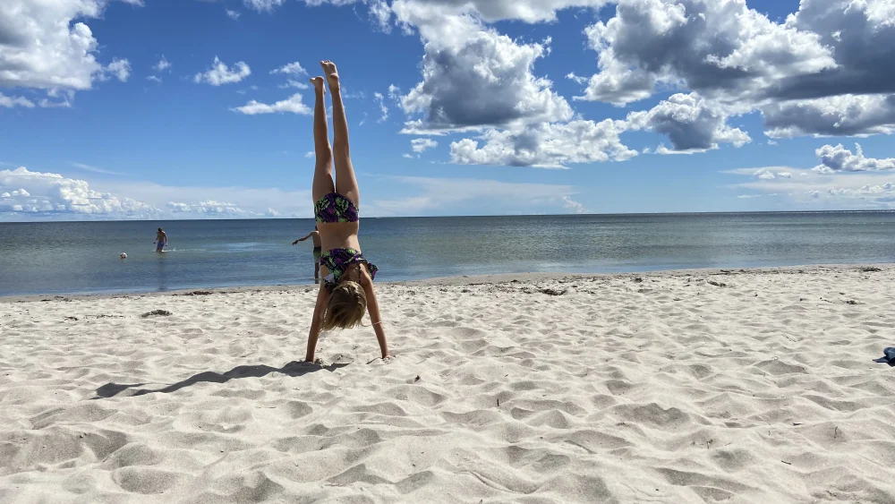 Ett barn står på händer på en sandstrand.