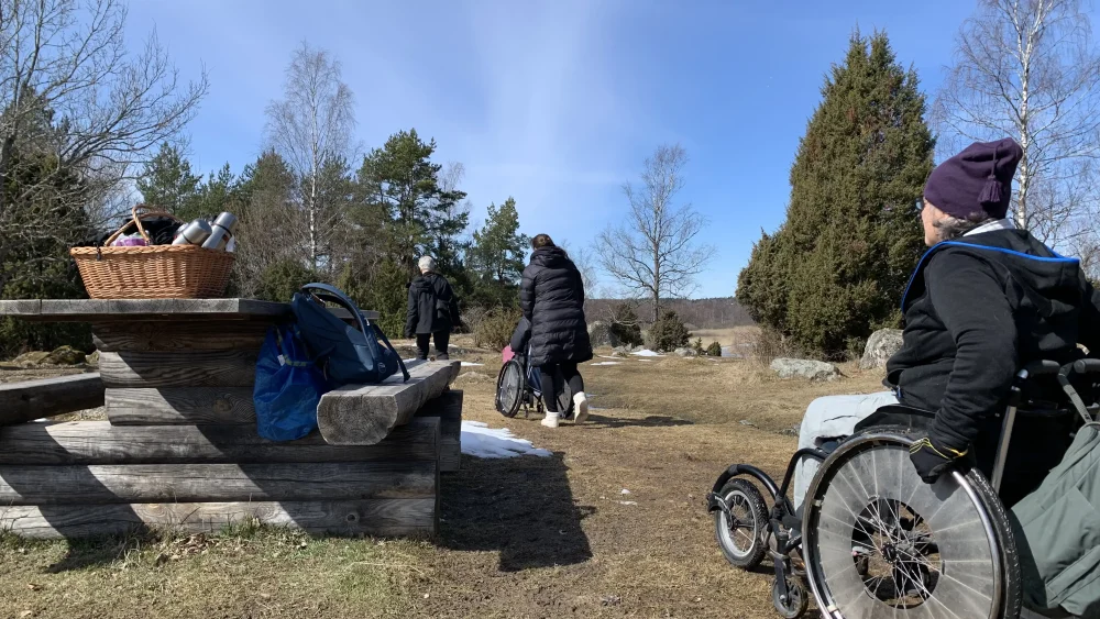 En person i rullstol bredvid ett bänkbord. Hagmark på våren.
